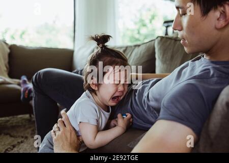Vater auf Vaterschaft verlassen Blick auf männliche Kleinkind weinend in Wohnzimmer Stockfoto