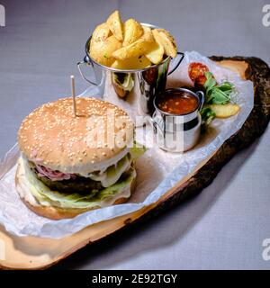 Burger und Pommes mit Sauce und Tomaten auf einem Holz Teller in einem Restaurant Stockfoto