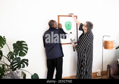 Seniorenpaar hängt zu Hause Malerei an der Wand Stockfoto