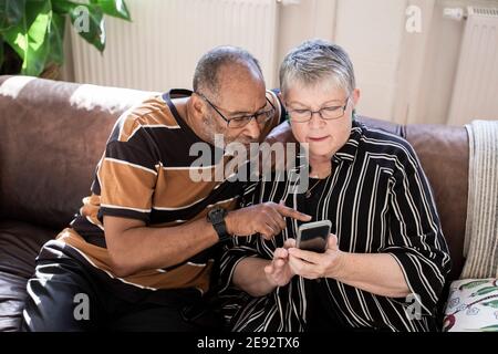 Ältere Paare, die im Wohnzimmer ein Smartphone benutzen Stockfoto