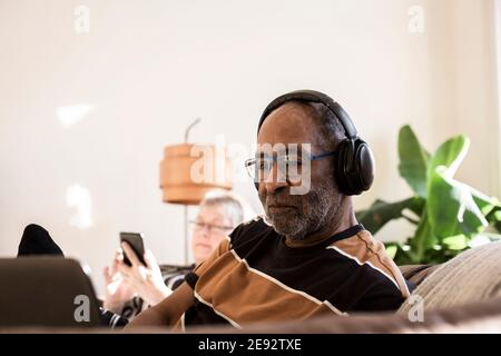 Älterer Mann mit Kopfhörern mit Laptop zu Hause Stockfoto