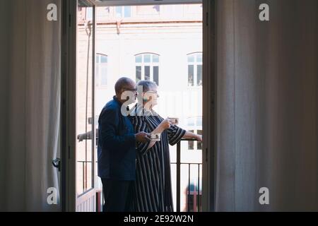 Seniorenpaar mit Kaffeetasse, die zu Hause auf dem Balkon stehen Stockfoto