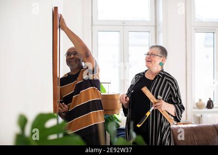 Lächelndes Seniorenpaar, das zu Hause Gemälde an die Wand hängt Stockfoto