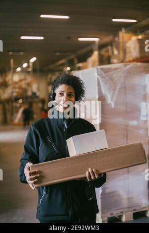 Lächelnde Geschäftsfrau mit Headset, die Pakete im Lager hält Stockfoto