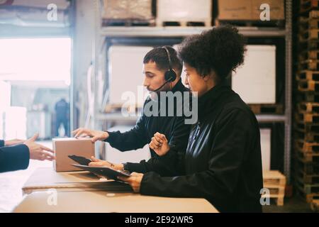 Männliche und weibliche Mitarbeiter mit Paket im Distributionslager Stockfoto