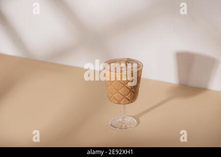 Kaffee in einem Glas auf beigem Hintergrund mit Schatten Stockfoto