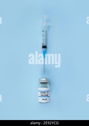 Einmalspritze und medizinische Flasche mit Coronavirus-Impfstoff auf blauem Hintergrund. Stockfoto