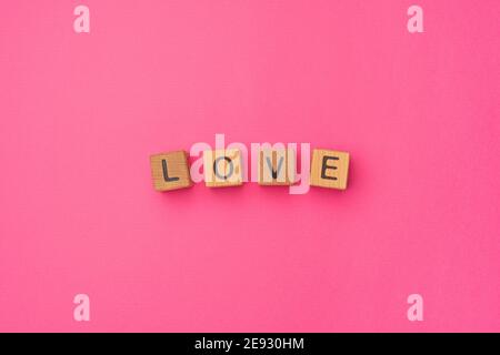 Holzwürfel mit dem Wort Liebe auf einem leeren bunten rosa Hintergrund. Wort der Liebe sind aus Briefen aus Holz für Ihre Freundin, Freund, Frau, Mann, für Valentinstag Gruß romantische Postkarte. Flach liegend, Draufsicht Stockfoto