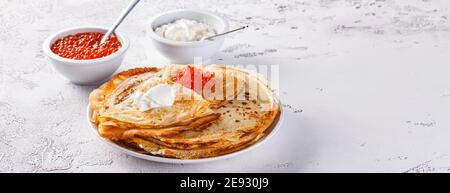 Traditionelle russische Crepes Blini stapelten sich in einer Platte mit rotem Kaviar, frischer saurer Sahne auf hellem Hintergrund. Maslenitsa traditionelles russisches Festival MEA Stockfoto