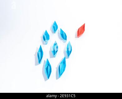 Gruppe von blauen Papierbooten in eine Richtung und ein rotes Papierboot, das unterschiedlich auf weißem Hintergrund zeigt. Business für innovatives Lösungskonzept. Stockfoto