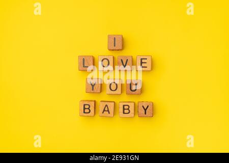 Holzwürfel mit der Phrase I Love You Baby auf einem leeren bunten gelben Hintergrund. Worte der Liebe sind aus Briefen aus Holz für Ihre Freundin, Freund, Frau, Mann, für Valentinstag Gruß romantische Postkarte. Flach liegend, Draufsicht Stockfoto
