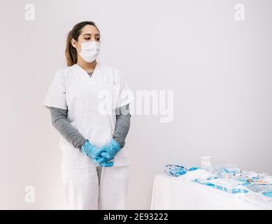 Ernsthafte weibliche Sanitäter in Schutzmaske und Handschuhe in der Nähe stehen Tabelle mit verschiedenen Geräten für die Coronavirus-Diagnose Stockfoto