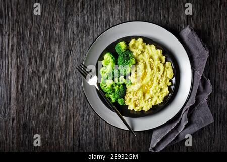 Brokkoli Kartoffelbrei bestreut mit gehackten Mandeln serviert mit gedünsteten Brokkoli-Röschen auf einem schwarzen Teller auf einem dunklen Holztisch, horizontale Ansicht von Stockfoto