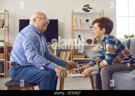 Fröhlicher Großvater und kleiner Enkel spielen Dame und Spaß haben Zu Hause Stockfoto