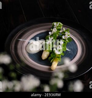 Gericht gekochten weißen Spargel plattiert und mit Weiß dekoriert Blumen und Sahne auf der Seite in einem Restaurant Stockfoto