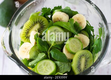 Vor der Wand wurden grünes Obst und Gemüse und ein gesundes Getränk zubereitet. Der Prozess der Zubereitung von grünen Smoothiein einer Küche Mixer Stockfoto