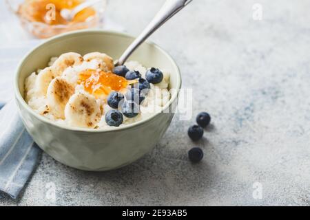 Frühstück mit Milchreis Porridge mit Banane, Heidelbeere und Orangenmarmelade, cremiger Reispudding oder französisch riz au lait in einer Schüssel. Für Text platzieren Stockfoto