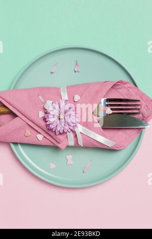 Schöne festliche Tischdekoration mit grünem Teller, Serviette, Blumen und Herzen auf pastellrosa und grünem Hintergrund. Draufsicht mit Kopierbereich. Stockfoto