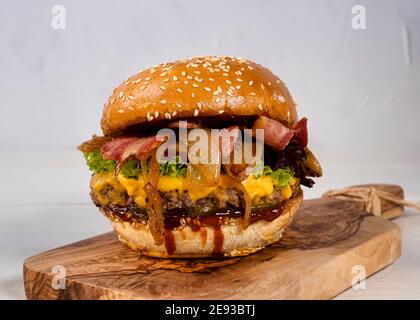 Saftiger Käse-Burger mit Rind und Speck, Tomaten, Gurken und Zwiebeln schön auf einem Holzbrett auf weißem Hintergrund angeordnet Stockfoto