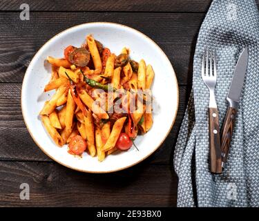 Rigatoni arrabiata mit feuriger Tomatensauce auf braunem Holz Tisch mit Gabel und Messer Stockfoto