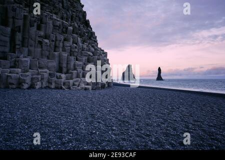 Der schwarze Lavasandstrand von Reynisfjara und der Reynisdrangar Basaltmeer stapelt sich in der Dämmerung an der Südküste Islands - Isländische Basaltlandschaft Stockfoto