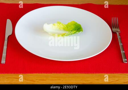 Weight Loss Dietierung kalorienarme Einzelsalat Blatt auf weiß Teller Besteck auf rotem Stoffhintergrund mit Holztisch Stockfoto