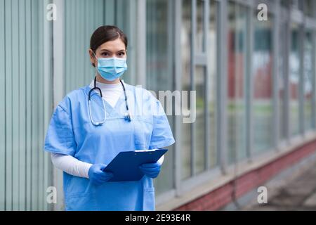 Portrait von müde erschöpft weibliche kaukasischen NHS Schlüssel Arzt in Vorderseite der Klinik oder des Krankenhauses, Coronavirus-Patiententriage für COVID-19-Virus Krankheit, Globen Stockfoto