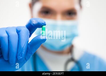 Weibliche UK NHS GP Hausarzt Arzt trägt schützende Gesicht Maske, blaue Handschuhe, hält grüne Pille, selektive Detail Fokus, Patienten Heilung und remed Stockfoto