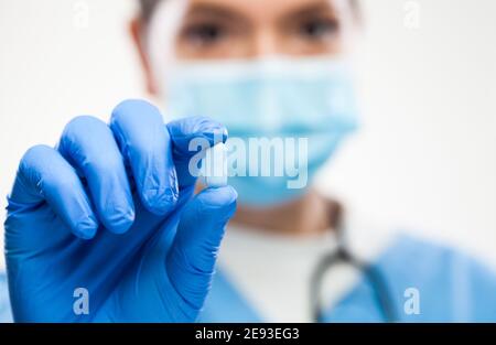 Weibliche UK NHS GP Hausarzt Arzt trägt schützende Gesicht Maske, Handschuhe, hält blaue Pille, selektive Makro Detail Fokus, Patienten Heilung und remed Stockfoto