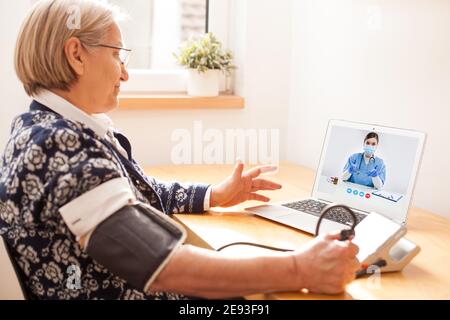 Ältere ältere Rentnerin mit Blutdruckmessgerät zur Verwendung Messung des Herzfrequenzpulses, Gespräch mit weiblicher E-Ärztin über Online-Video kal Stockfoto
