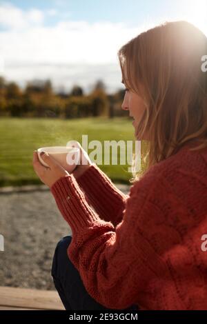 Junge Frau, die auf der Veranda sitzt und Kaffee trinkt Stockfoto