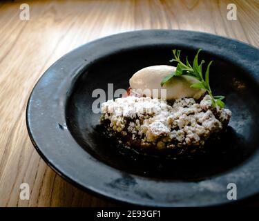 Platte aus Sorbet und Rhabarber Pie mit Minzblättern bedeckt In einer schwarzen Schale auf einem Holztisch in einem Restaurant Stockfoto