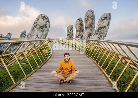 Junger Mann Tourist tun Yoga auf einer berühmten Touristenattraktion - Goldene Brücke an der Spitze der Ba Na Hills, Vietnam Stockfoto