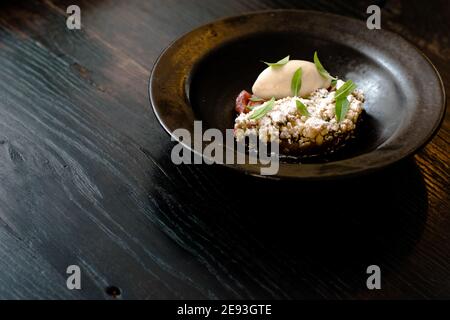 Platte aus Sorbet und Rhabarber Pie mit Minzblättern bedeckt In einer schwarzen Schale auf einem Holztisch in einem Restaurant Stockfoto