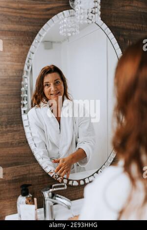 Ältere Frau reflektiert im Badezimmerspiegel Stockfoto
