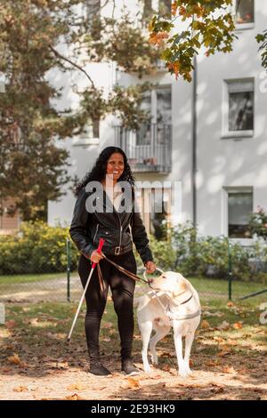 Sehbehinderte Frau lächelt und hält Blindenhund Stockfoto