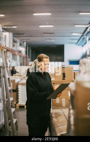 Reife manuelle Arbeiterin, die Pakete im Logistiklager analysiert Stockfoto