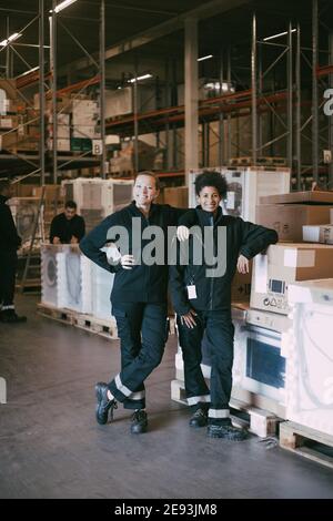 Glückliche weibliche Kollegen stehen bei Boxcontainern im Lager Stockfoto