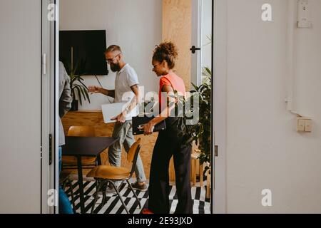 Männliche und weibliche Kollegen mit Laptop im Vorstandszimmer gesehen Durch den Eingang des Büros Stockfoto