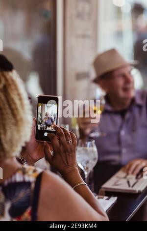 Zugeschnittenes Bild einer Frau, die einen Mann fotografiert, während sie im Café sitzt Stockfoto