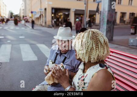 Ältere Paare essen, während sie auf der Bank in der Stadt sitzen Stockfoto