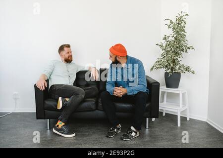 Männliche Mitarbeiter sitzen und sprechen auf dem Sofa Stockfoto