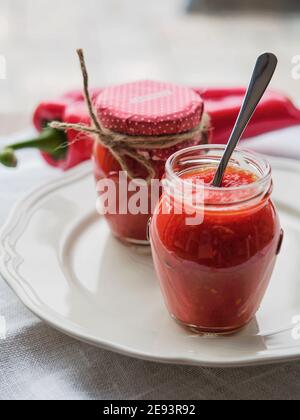 Ajvar, traditionelle Balkan gerösteten roten Pfeffer genießen im Glas mit Löffel auf weißem Teller und Hintergrund. Geringe Schärfentiefe. Stockfoto