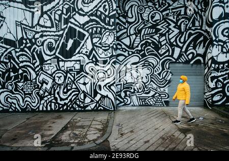 Eine Frau mit Gesichtsbemalung geht an einem Graffiti-Wandgemälde (unbekannter Künstler) an einer Wand in der Lancefield Street in Glasgow vorbei, während die Stadt im Lockdown bleibt. Stockfoto