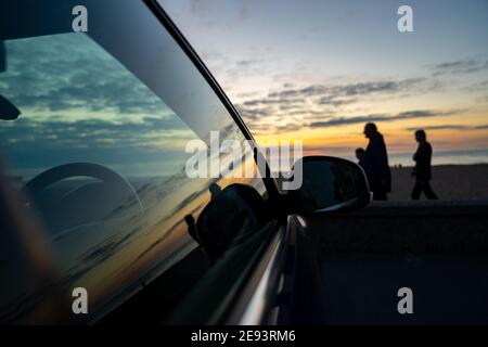 Sommer Sonnenuntergang am Strand während im Urlaub Urlaub reflektierend In der Seite des Autofensters Glas mit Silhouette der Familie Leute, die wunderbar laufen Stockfoto