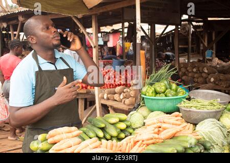 Ein afrikanischer Marktmann, der Obst und Gemüse verkauft und ein Telefonanruf Stockfoto