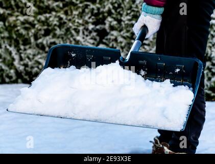 Nahaufnahme einer Person, die mit einer Schneeschaufel Schnee vom Bürgersteig räumte. Stockfoto