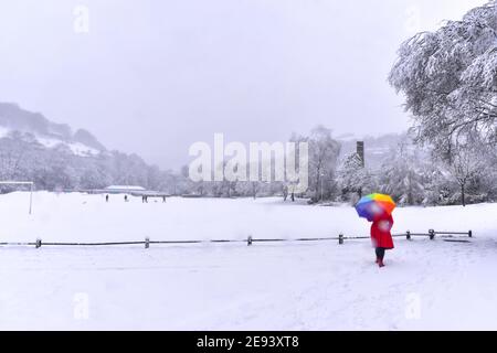 Frau im roten Mantel und farbigen Regenschirm beim Wandern im Schnee, Calder Holmes Park, Hebden Bridge, Calderdale, West Yorkshire Stockfoto