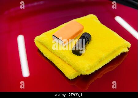 Nahaufnahme eines Beschichtungssets: mikrofaser, Schwamm-Applikator und Flüssigglas-Nano-Schutz auf eine Autohaube auftragen. Vorbereitung für die Anwendung Spezial Stockfoto