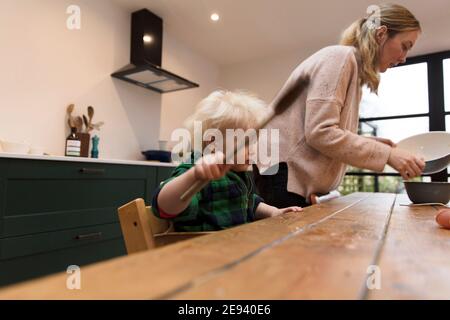 Ein Kleinkind hilft, einen Kuchen mit einem großen Spatel zu backen. Stockfoto